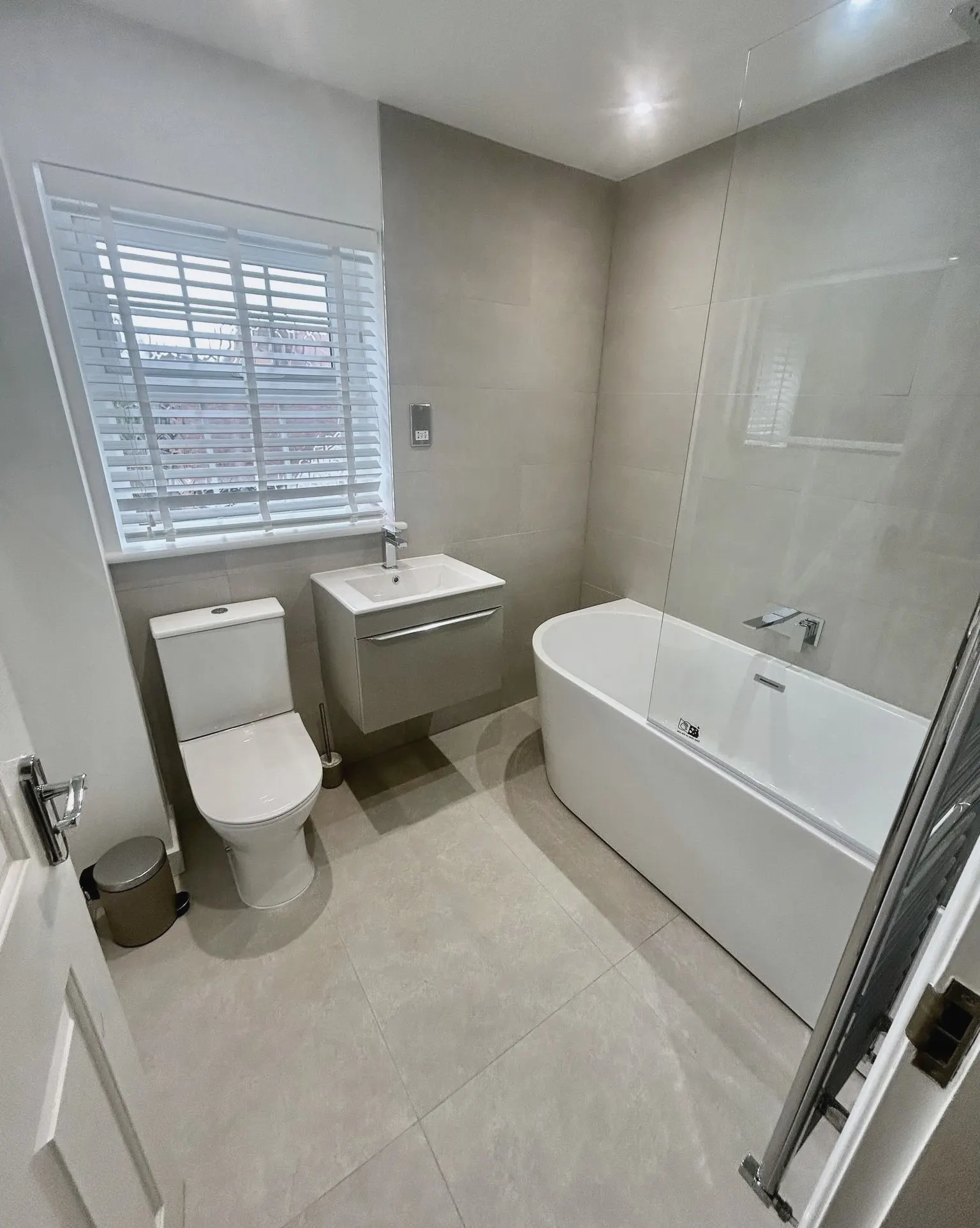 Bathroom with a fitted bath and glass screen, a wall-hung basin and white window shutters