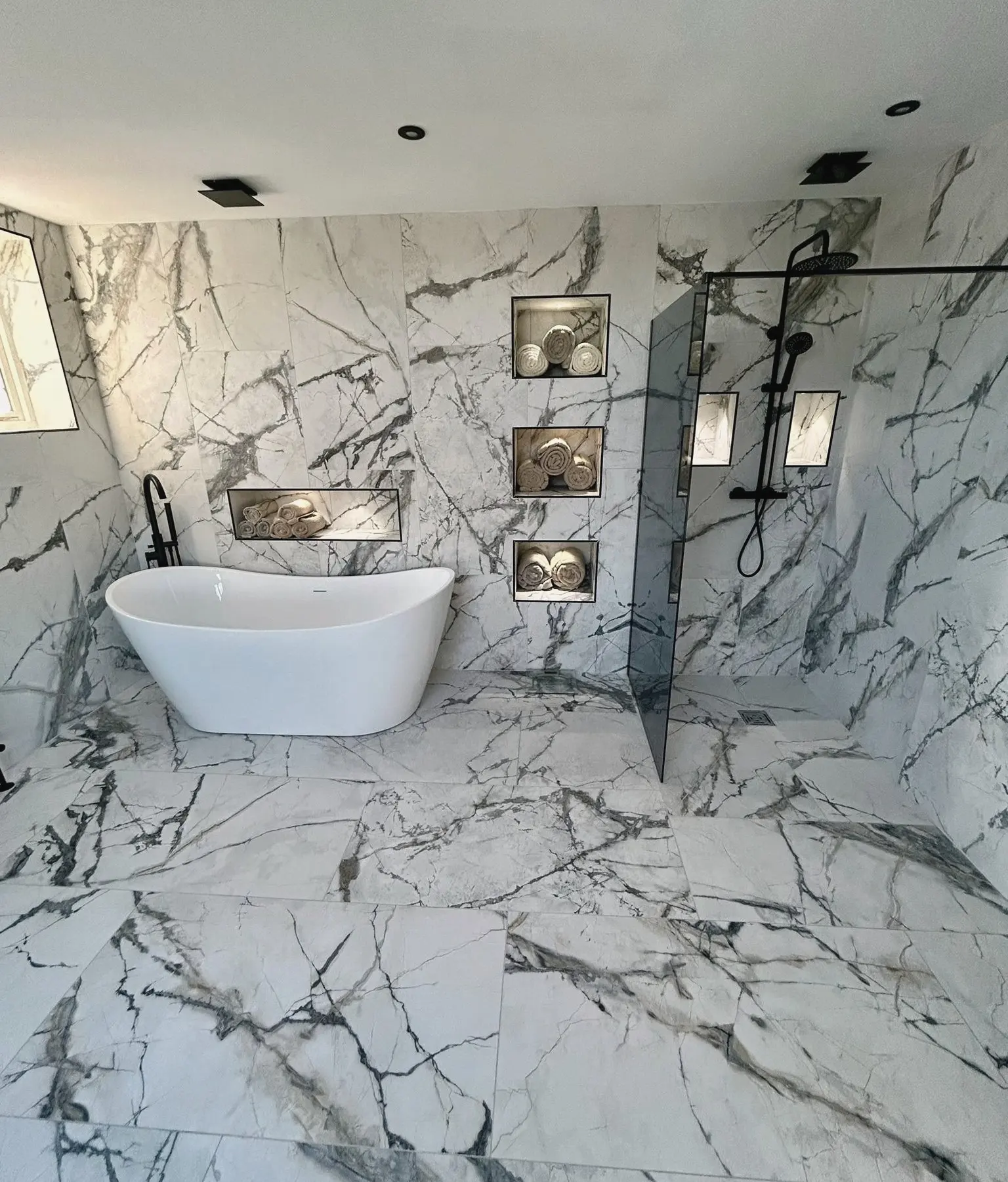Bathroom tiled in marble-effect porcelain, with a freestanding bath, lit recessed shelves and a walk-in shower