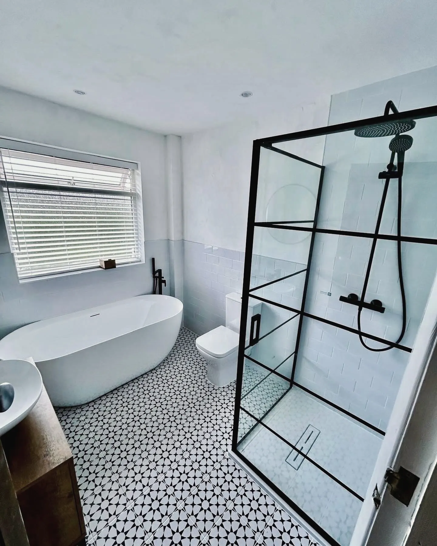 Bathroom with a freestanding bath, a black-framed shower screen and patterned floor tiles