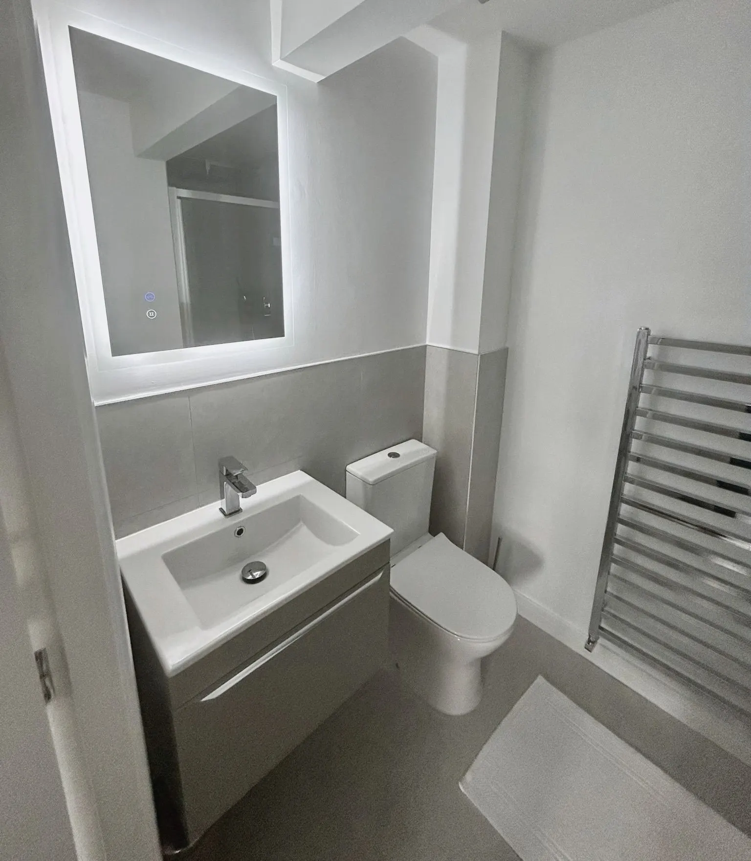 Illuminated mirror above a wall-hung vanity basin, with a chrome towel radiator