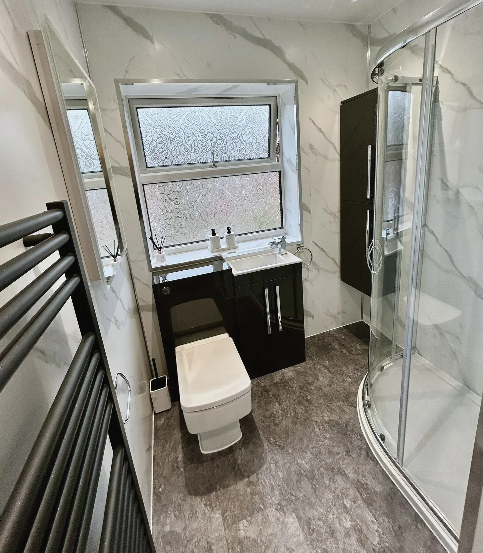 Quadrant shower enclosure with marble-effect wall panels and a dark vanity unit