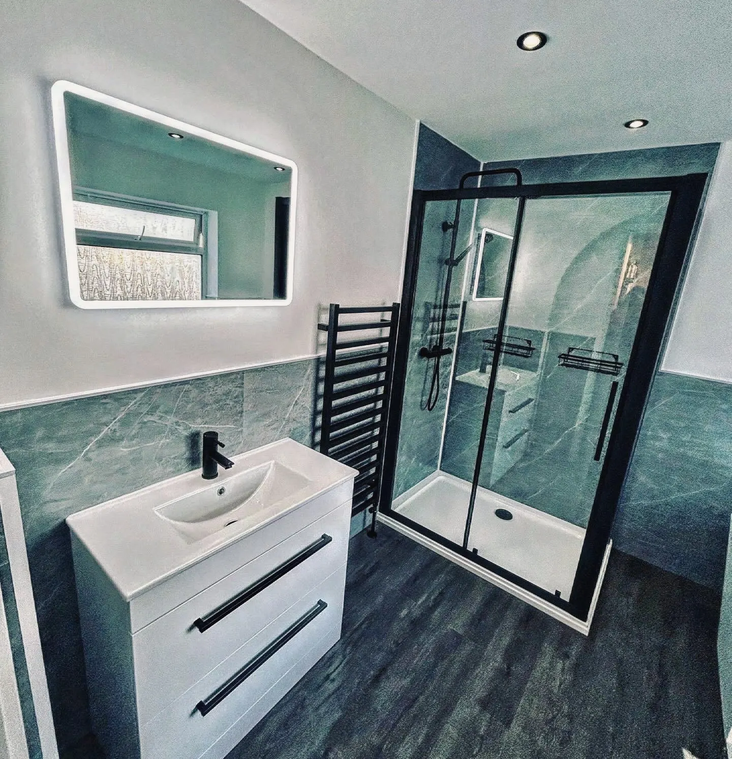 Wall-hung vanity unit beneath an illuminated mirror, beside a shower enclosure
