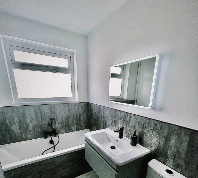 Bathroom with a window, an illuminated mirror, a wall-hung basin and a fitted bath