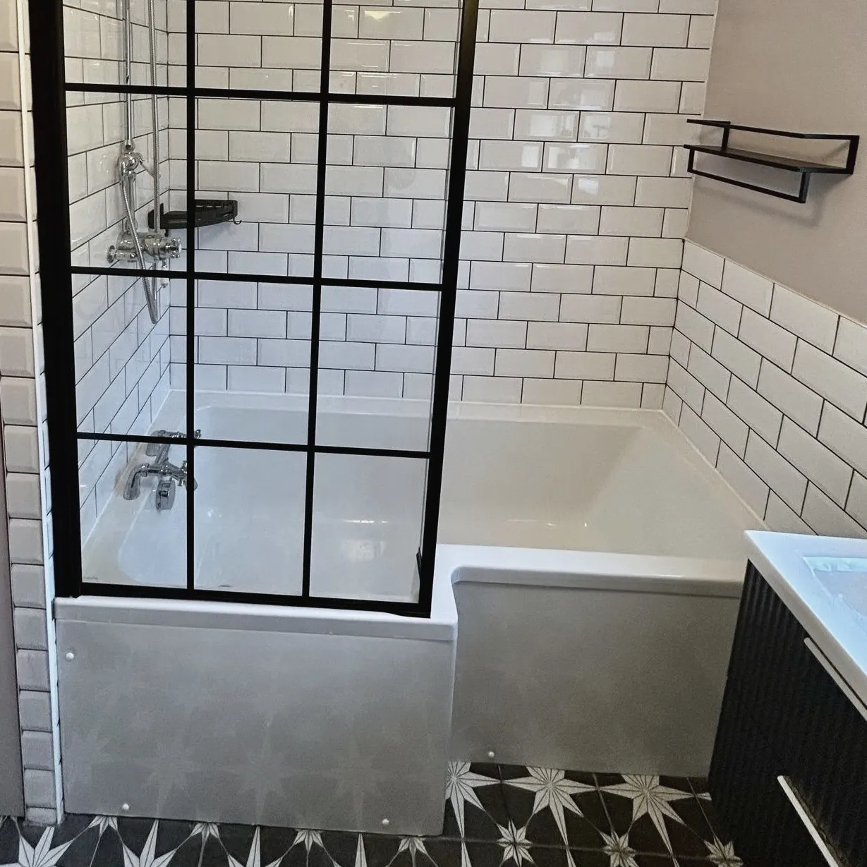 White metro wall tiles with dark grout behind a black-framed bath screen
